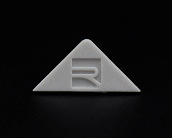 Szary, trójkątny obiekt na czarnym tle z wytłoczonym literą 'R' w środku.