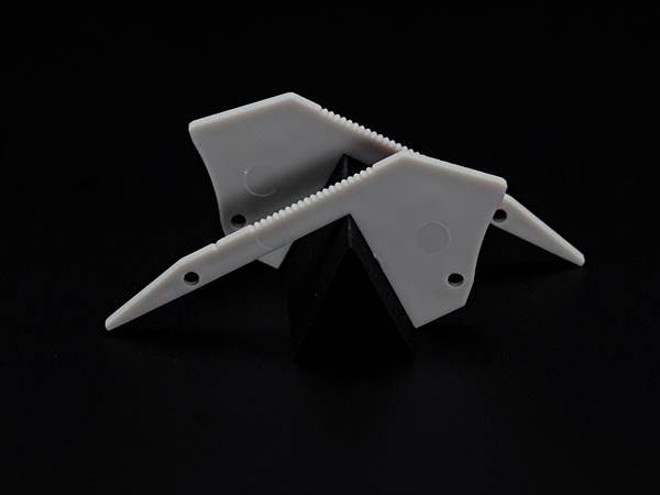 Abstrakcyjny model wykonany z białego tworzywa sztucznego przedstawia geometryczne kształty spoczywające na czarnym obiekcie o kształcie piramidy.