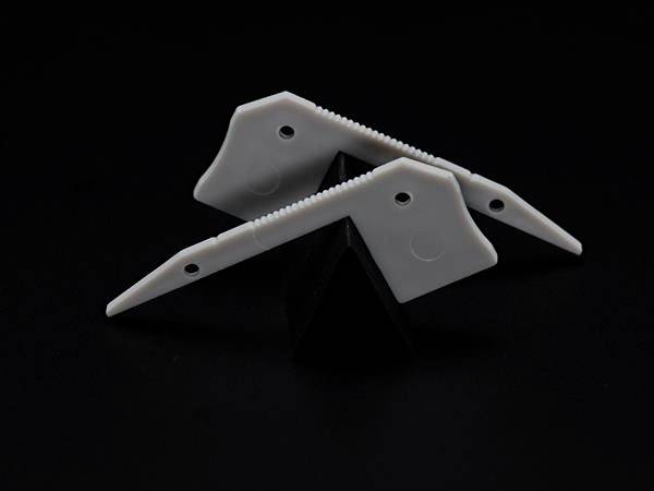 Dwa białe plastikowe elementy z zębami, balansujące na czarnym trójkątnym obiekcie, na ciemnym tle.