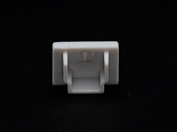 Biały plastikowy hak na czarnym tle. Hak ma kształt kwadratu z dwoma uchwytami po bokach.