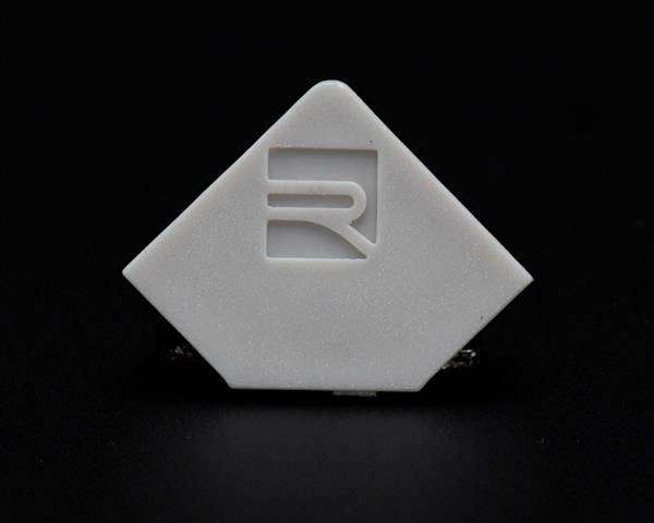 Biały, rombowaty obiekt z wygrawerowanym stylizowanym symbolem na ciemnym tle.