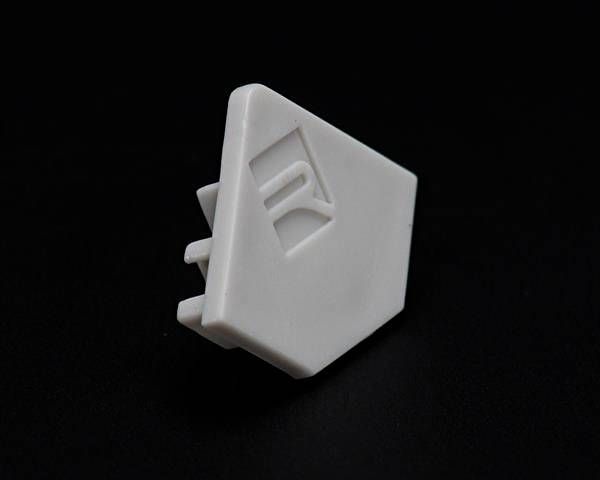 Biały, trójkątny element z tworzywa sztucznego z trzema wystającymi bolcami i wypukłą cyfrą '1', na czarnym tle.