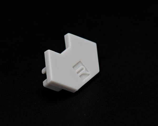 Mały, biały, prostokątny kawałek plastiku z wygrawerowaną linią. Leży na ciemnym tle.