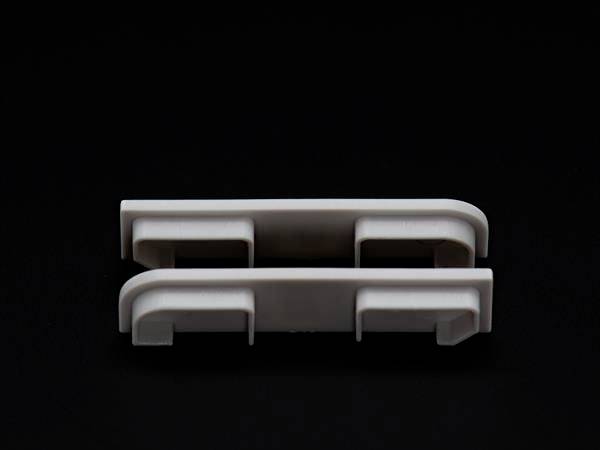 Dwa białe, podłużne plastikowe klipsy na czarnym tle, ułożone jeden na drugim.