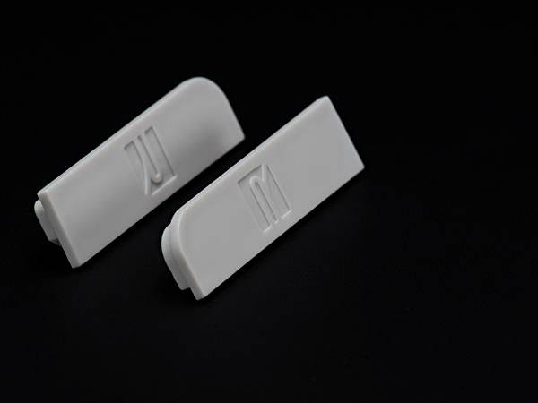 Dwa białe plastikowe spinacze leżą na czarnym tle, jeden z zagiętą krawędzią, drugi z prostą krawędzią.