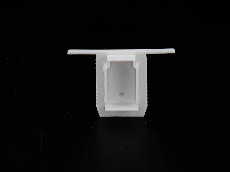Biała komponenta z tworzywa sztucznego z prostokątnym otworem pośrodku, na czarnym tle. Może być częścią większego urządzenia technicznego.