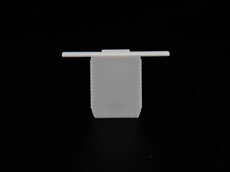 Biały plastikowy klips w kształcie litery T na czarnym tle.