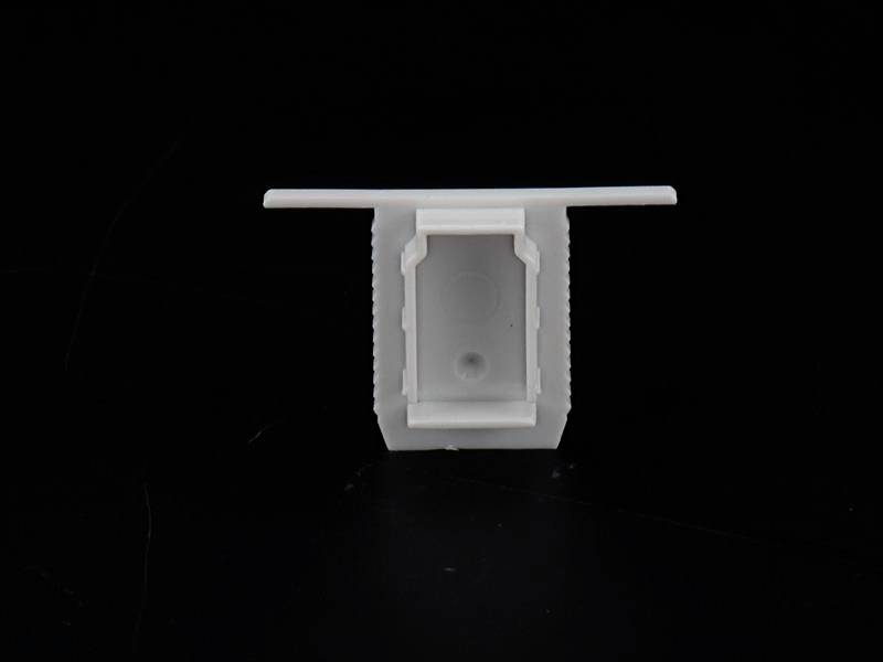 Kwadratowa, biała plastikowa nasadka na czarnym tle, prawdopodobnie pokrywka lub element adaptera.