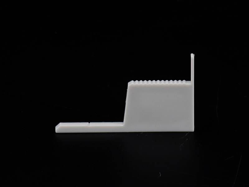 Biała, prostokątna plastikowa mocowanie z ząbkowanym końcem i małym występem na czarnym tle.
