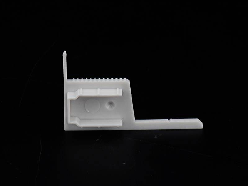 Biały plastikowy kąt na czarnym tle, prawdopodobnie element lub część mocująca, ukazuje swoje krawędzie i szczegóły strukturalne.
