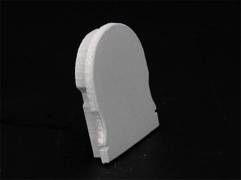 Prosty, biały element drewnianej układanki na czarnym tle, przedstawiający dolny segment profilu ludzkiej głowy.