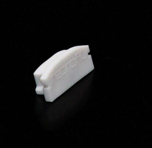 Biały obiekt z tworzywa sztucznego na czarnym tle, ukształtowany jak mała, zaokrąglona zakładka.