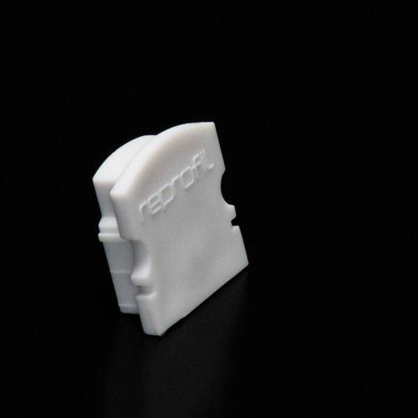 Biała łączówka z tworzywa sztucznego na czarnym tle, prawdopodobnie element systemu wtykowego lub złącza kablowego.