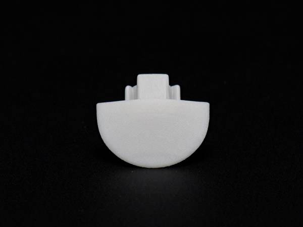 Biała, półokrągła komponenta z tworzywa sztucznego na czarnym tle, prawdopodobnie część jakiegoś urządzenia mechanicznego lub technicznego.