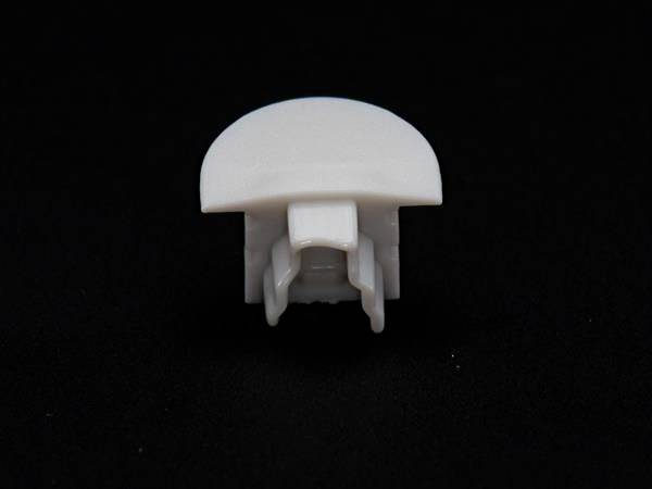 Biały element plastikowy, prawdopodobnie mocujący lub łączący, na czarnym tle.