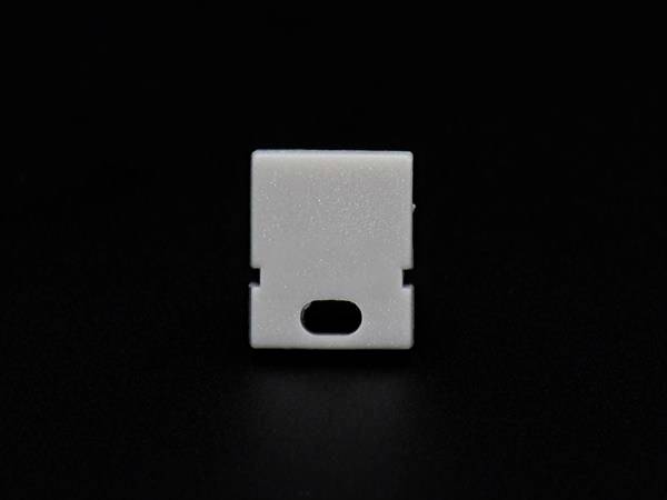 Biały kawałek plastiku na czarnym tle. Ma prostokątny kształt z owalnym otworem pośrodku u dołu.