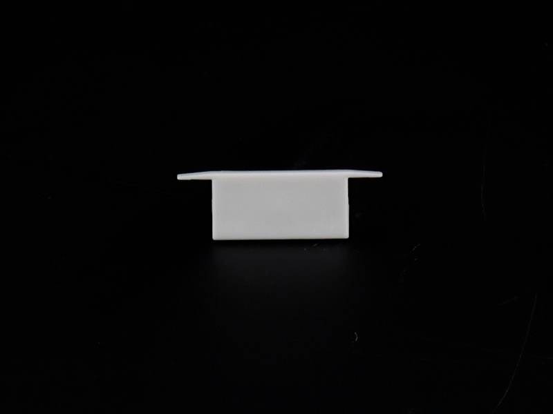 Mały, biały, prostokątny obiekt plastikowy z poziomymi kołnierzami na czarnej powierzchni.