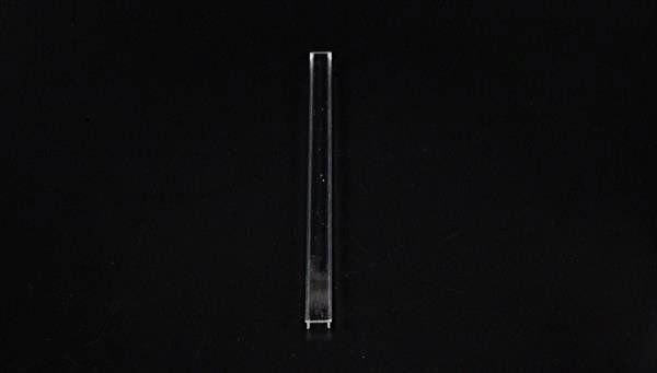 Pojedynczy, przezroczysty, wąski słup szklany stoi pionowo na czarnym tle.