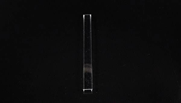 Podłużny, przezroczysty pojemnik szklany na czarnym tle.