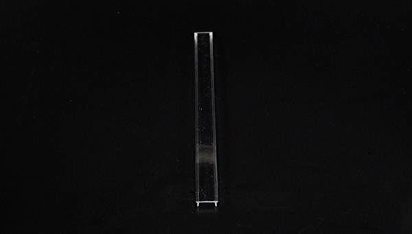 Pojedyncza, wąska szklana rurka stoi pionowo na czarnym tle.