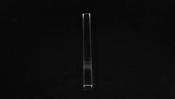 Cienki, przezroczysty szklany pręt stoi pionowo na czarnym tle.