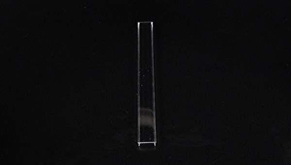 Pojedynczy, przezroczysty prostokątny pręt stoi pionowo na czarnym tle.