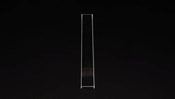 Prosty, wąski obiekt szklany (kuweta) stoi pionowo na czarnym tle. Jest używany do pomiarów przepuszczalności światła.