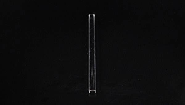 Przezroczysta szklana rurka stoi pionowo na czarnym tle.