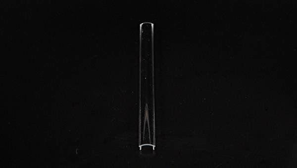 Na środku obrazu zawieszona jest przezroczysta, pusta probówka na czarnym tle.