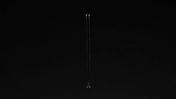Pojedynczy przezroczysty słomka przed czarnym tłem, ustawiona pionowo w centrum kadru.