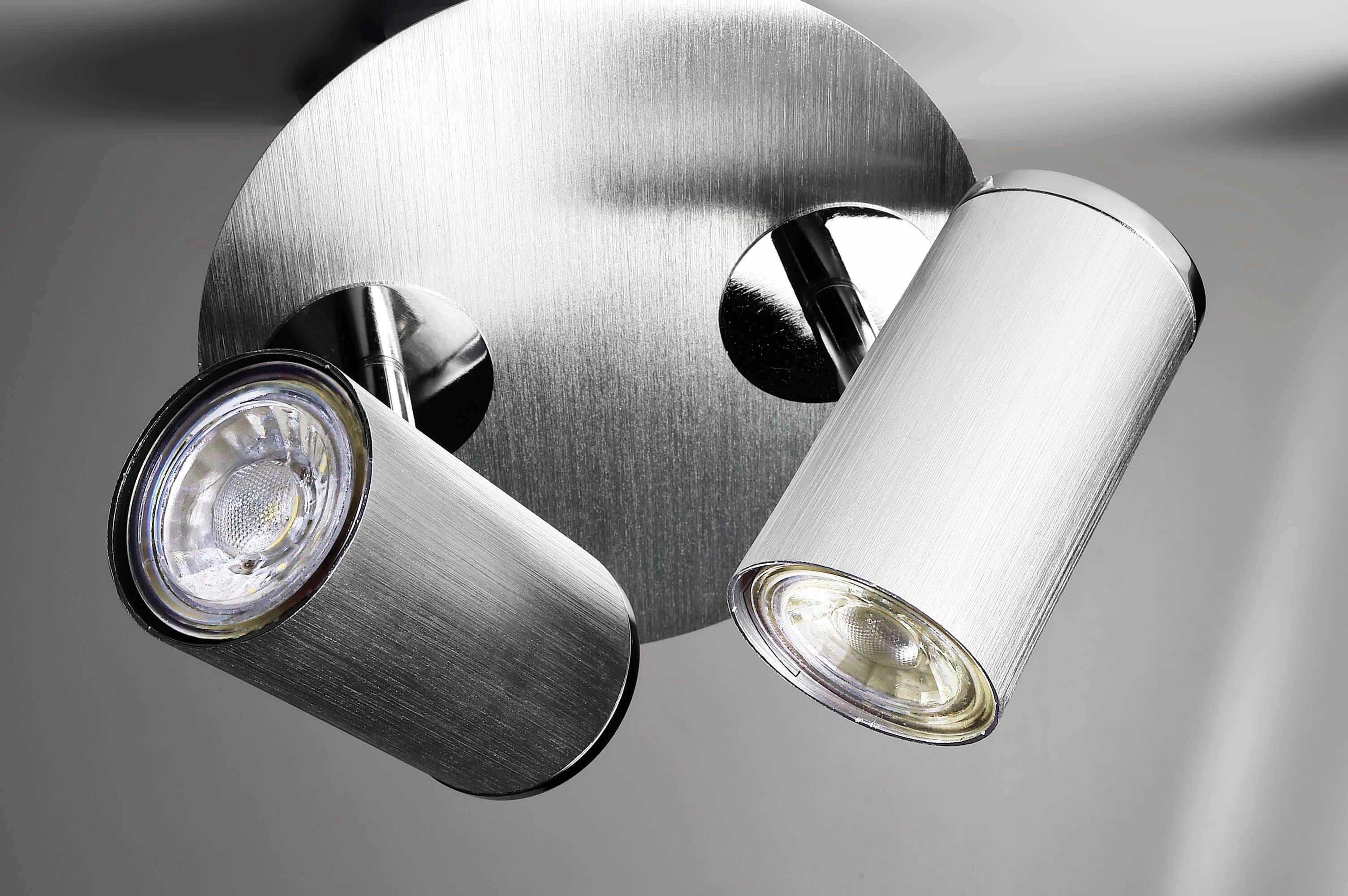 Dwa srebrzyste, cylindryczne reflektory sufitowe zamontowane na metalowej płycie. Świecą w dół, zapewniając precyzyjne oświetlenie.