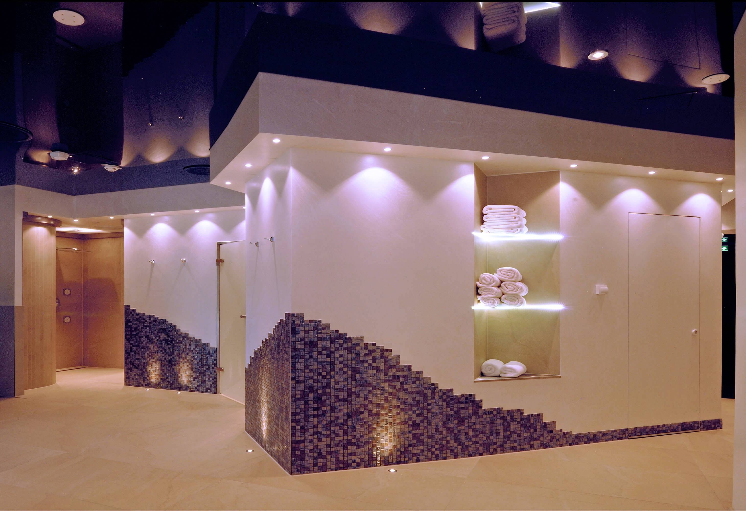 Nowoczesna, dobrze oświetlona strefa spa z półkami na ręczniki i dekoracyjnymi wzorami płytek na ścianach.