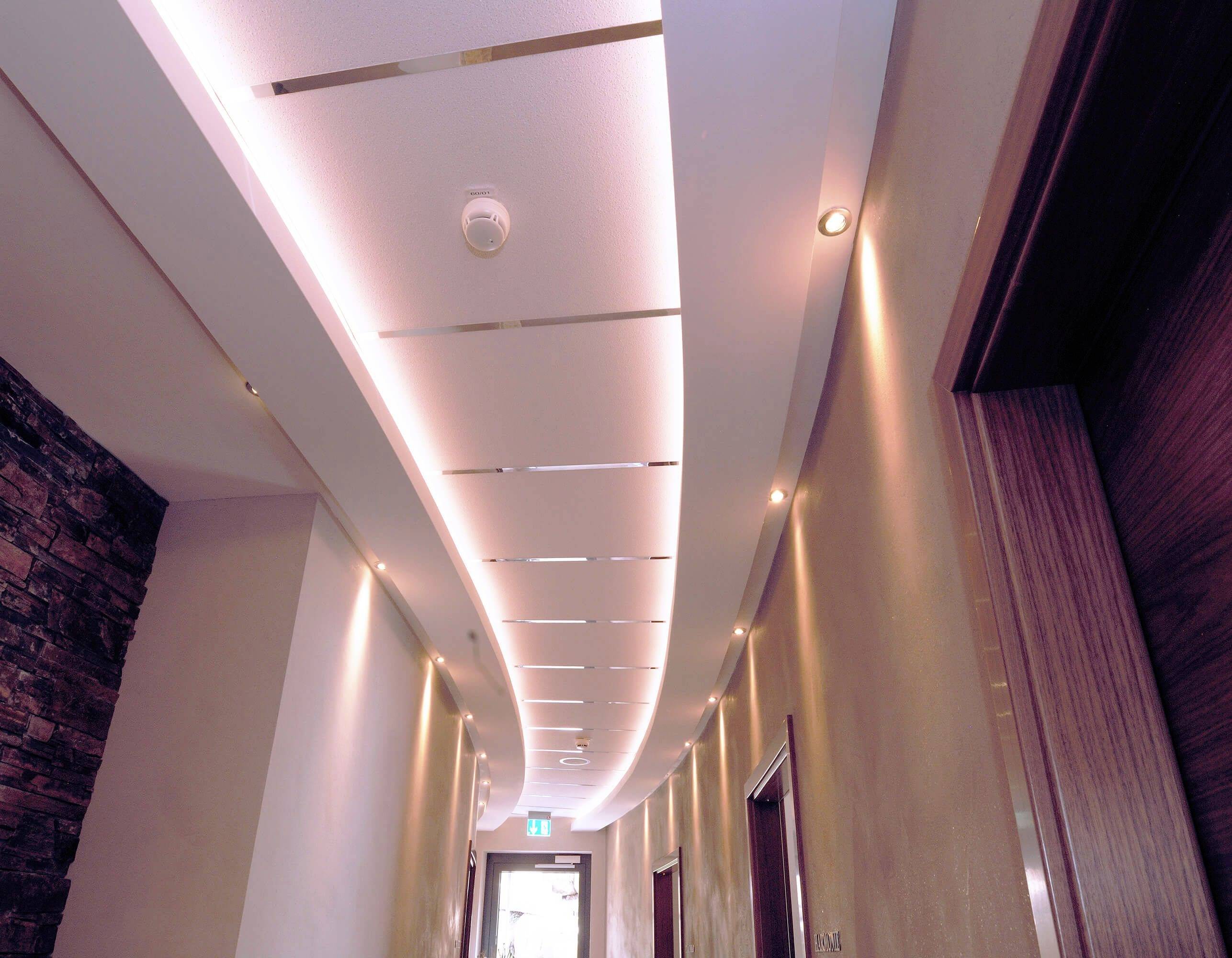 Elegancki korytarz z podświetleniem pośrednim na suficie i ścianach. Po prawej i lewej stronie znajdują się drzwi. W tle widać wyjście.