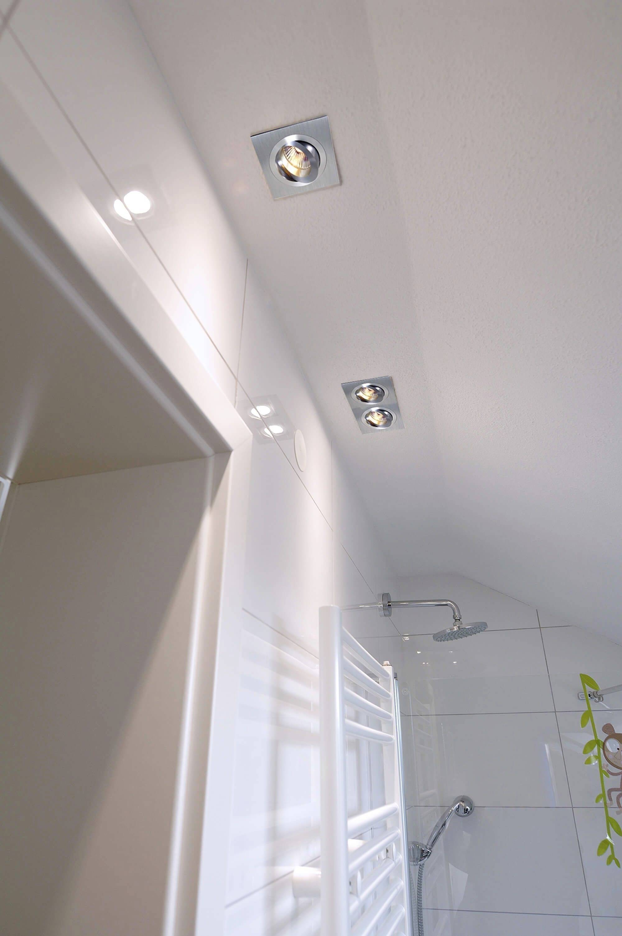 Łazienka wyłożona płytkami z natryskiem, grzejnikiem na ręczniki i trzema wpuszczonymi w sufit lampami. Dyskretna i nowoczesna.