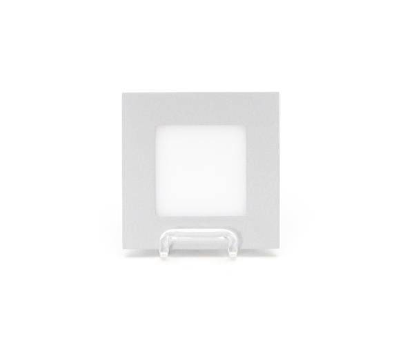 Kwadratowa, biała ramka na zdjęcia stoi centralnie na przezroczystej podstawce przed białym tłem.