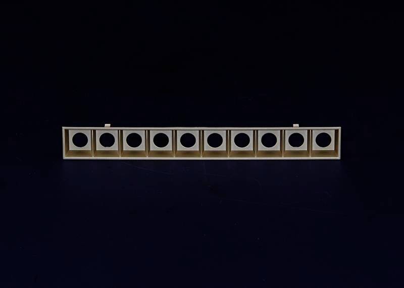 Drewniana listwa z dziewięcioma równomiernie rozmieszczonymi wzdłuż długości okrągłymi otworami, na ciemnym tle.
