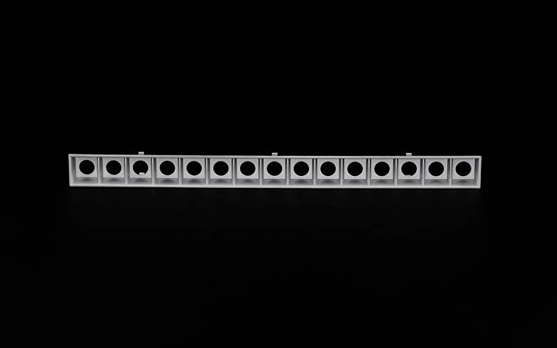 Długi, prostokątny element metalowy z wieloma okrągłymi otworami ułożonymi w rzędzie. Tło jest czarne.
