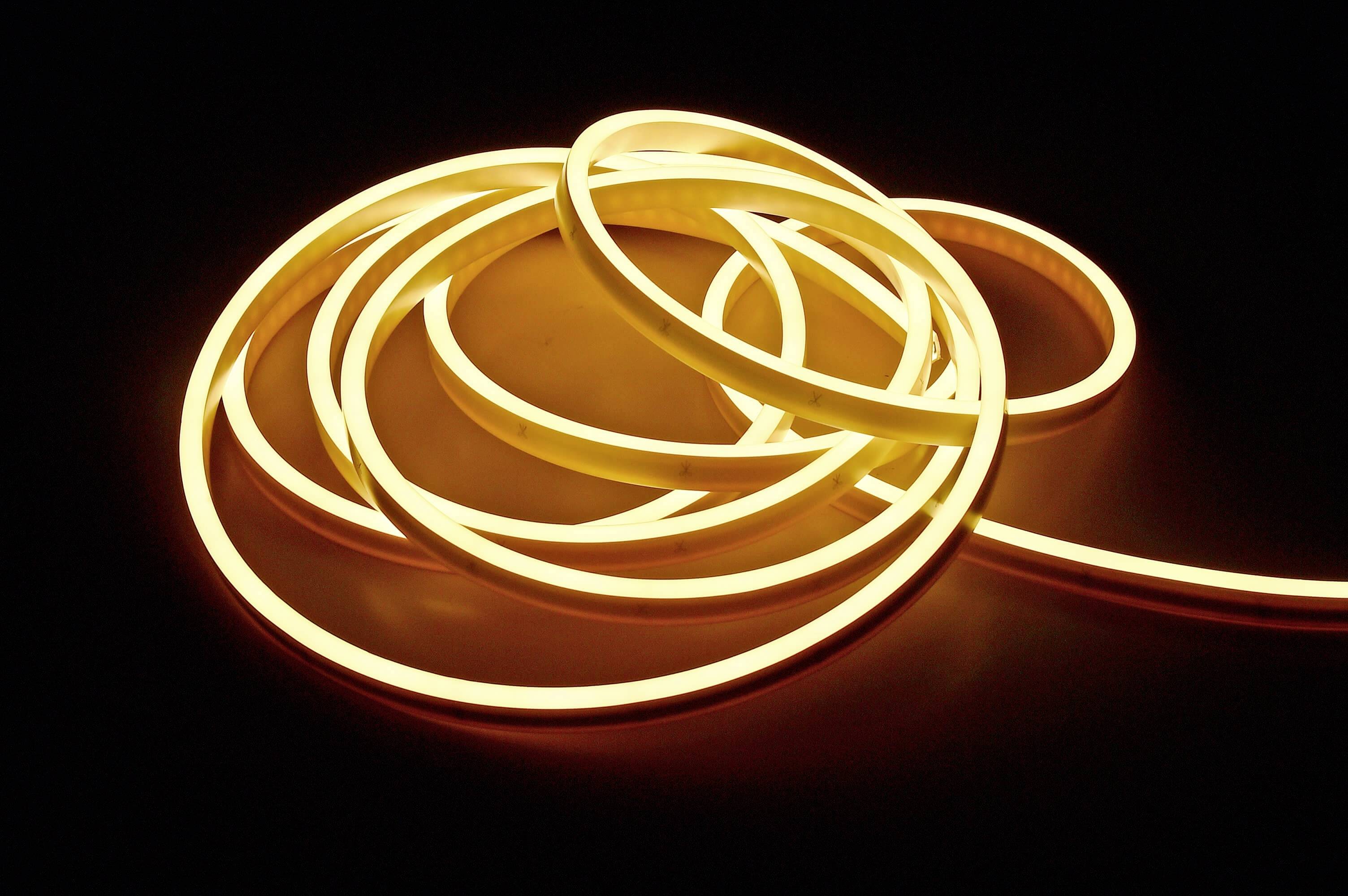 Długa, świecąca, żółtawo zabarwiona taśma LED wije się w nieregularnych pętlach na czarnym tle.