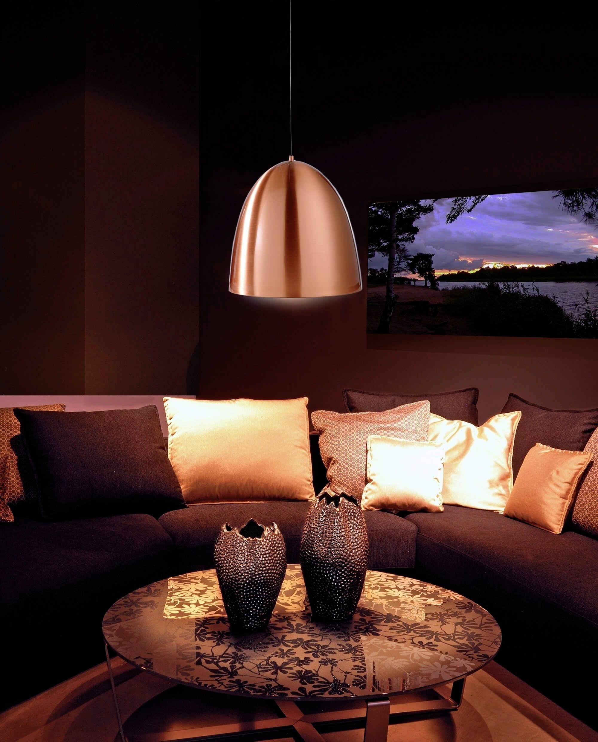 Salon z ciemnymi sofami i miedzianymi poduszkami. Okrągły stół z dekoracjami. Miedziana lampa ciepło oświetla pomieszczenie.