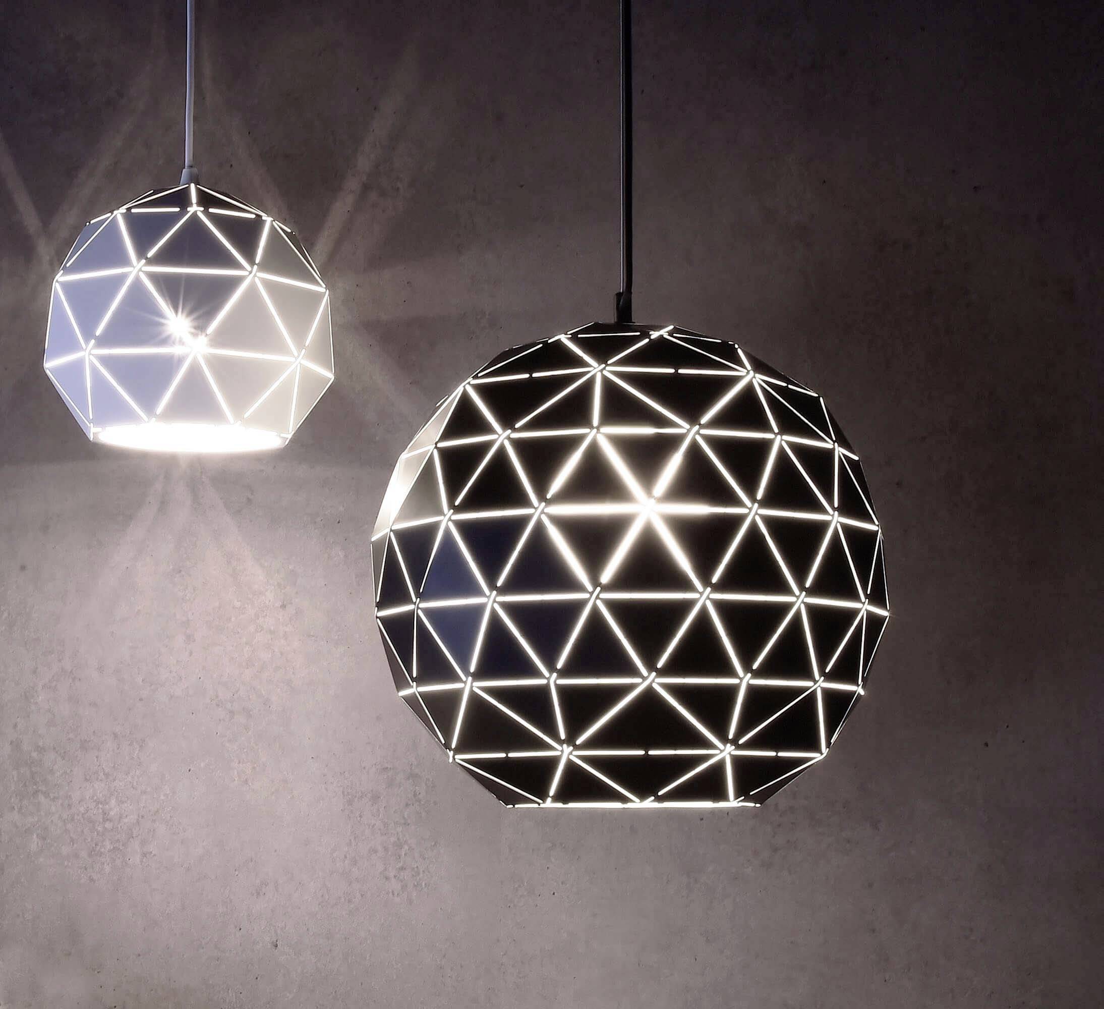 Dwie kulisté lampy sufitowe z geometrycznym wzorem świecą. Lewa lampa jest jaśniejsza od prawej.