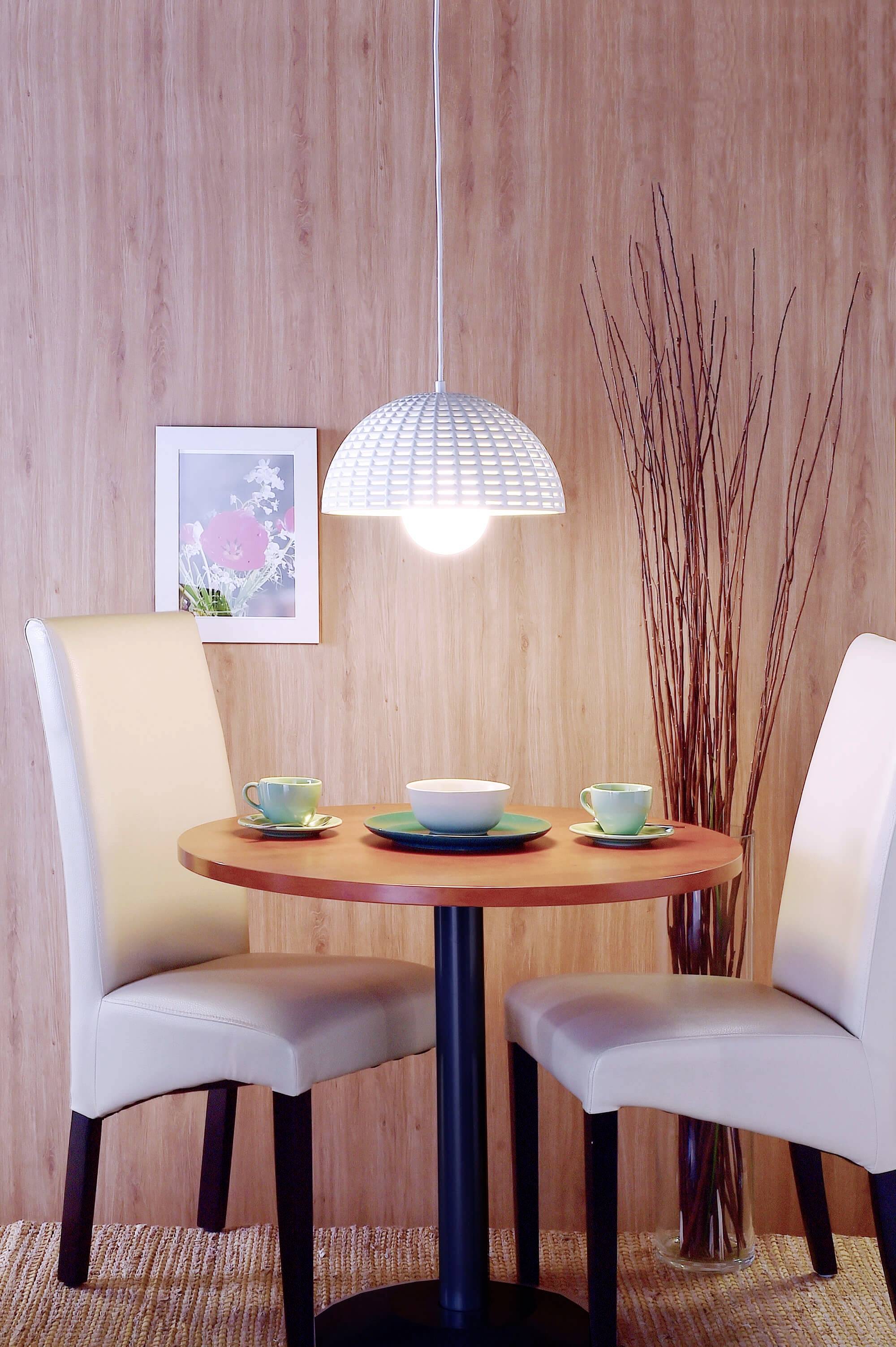 Dwa krzesła wokół okrągłego drewnianego stołu z filiżankami do herbaty i miskami, wisząca lampa nad nim, obraz i dekoracje w nowoczesnej jadalni.