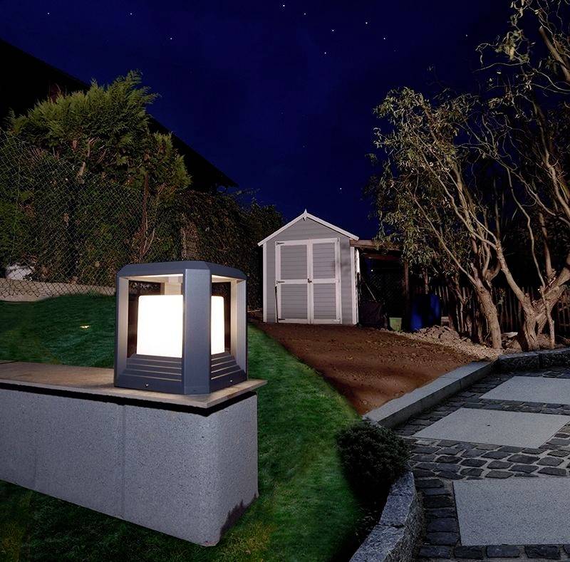 Ogród oświetlony latarnią na pierwszym planie. Po prawej stronie wybrukowana ścieżka. W tle szopa, otoczona drzewami nocą.