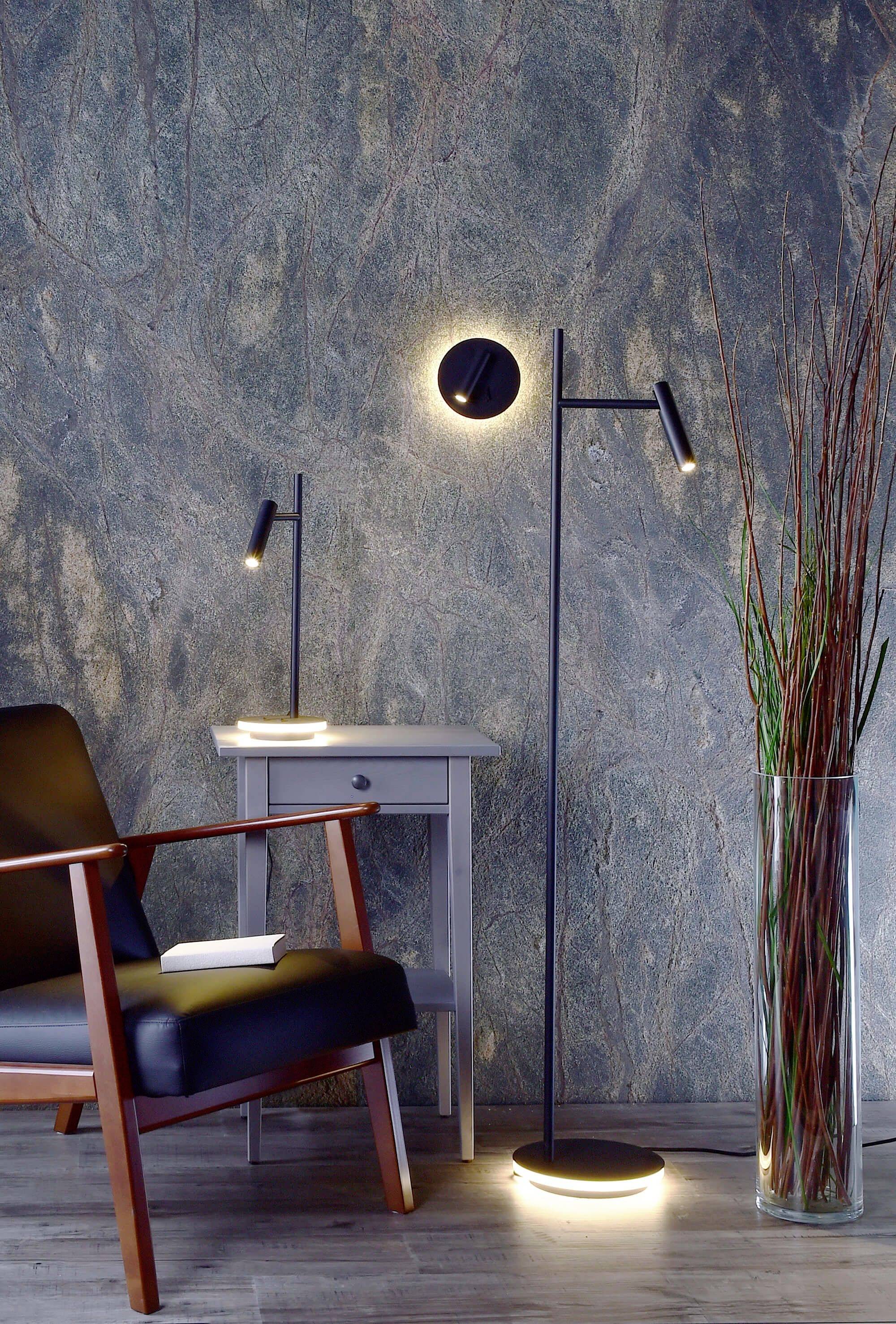 Stylowy pokój dzienny z fotelem, stolikiem pomocniczym i nowoczesnymi czarnymi lampami na tle wzorzystej ściany.