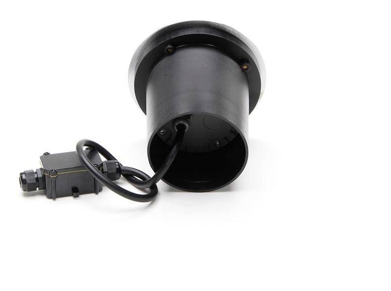 Czarny, cylindryczny korpus świetlny z przewodem i skrzynką przyłączeniową spoczywa na białej powierzchni, widziany pod skosnym kątem z tyłu.