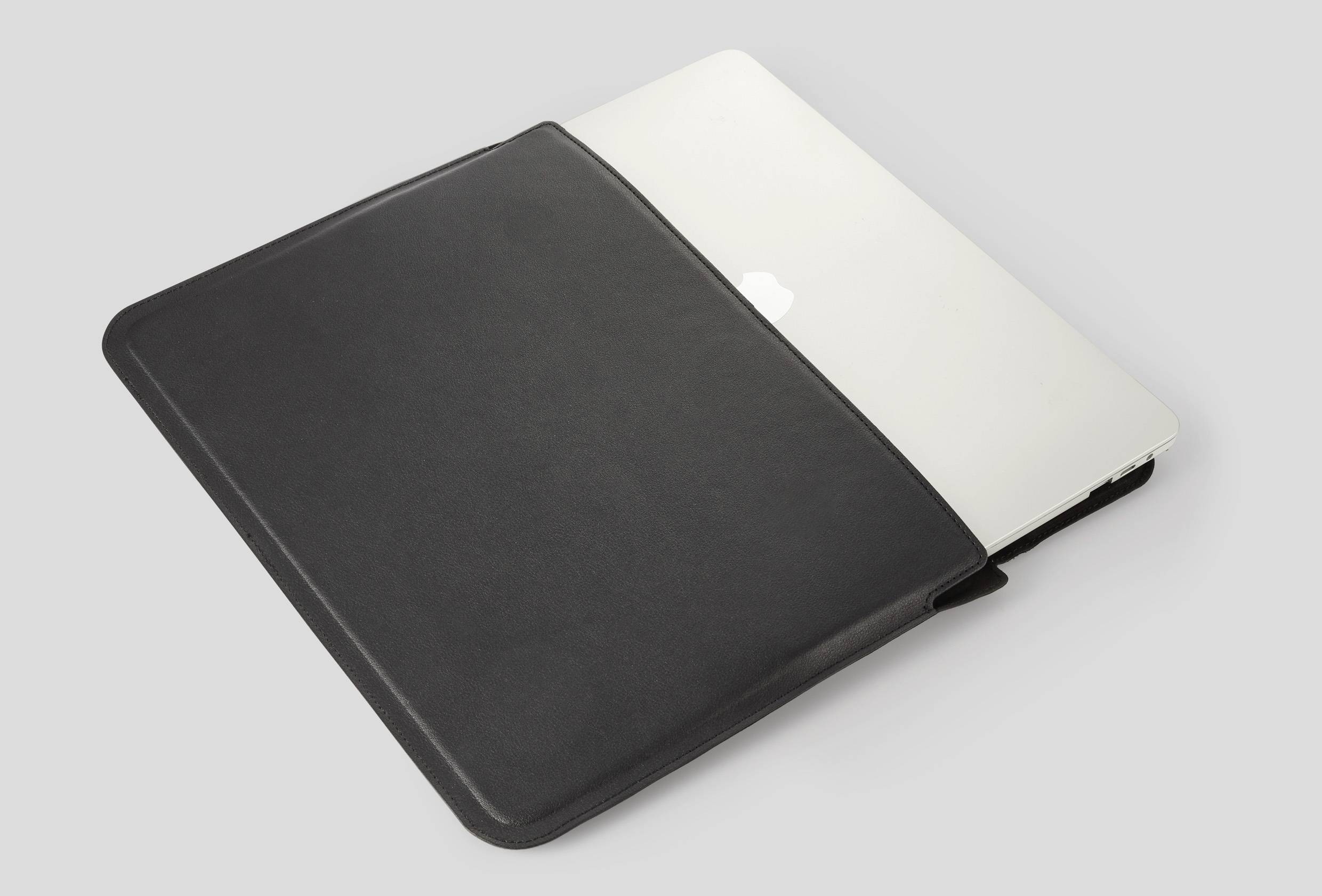 Laptop leży w czarnym etui na szarym tle.