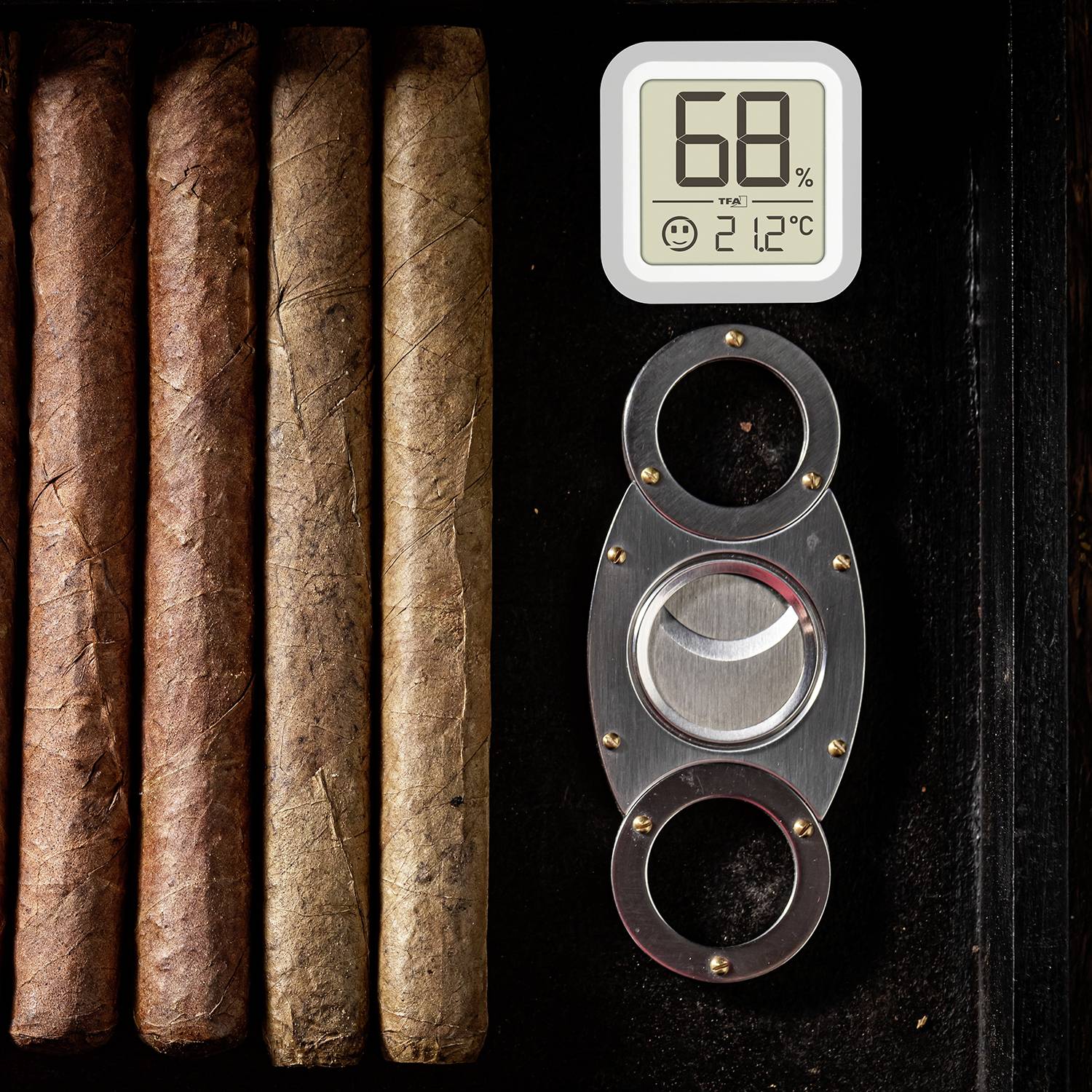 Kilka cygar leży obok cyfrowego higrometru, który wskazuje 68% wilgotności i 21,2 stopnia Celsjusza.