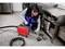Osoba używa narzędzia hydraulicznego do czyszczenia odpływu w kuchni komercyjnej, otoczona stalowymi blatem ze stali nierdzewnej i podłogą wyłożoną kafelkami.