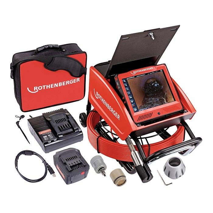 System inspekcji rur z czerwoną obudową, wyświetlacz pokazuje obraz kanału. W zestawie akumulator, ładowarka, kamera i akcesoria w torbie.