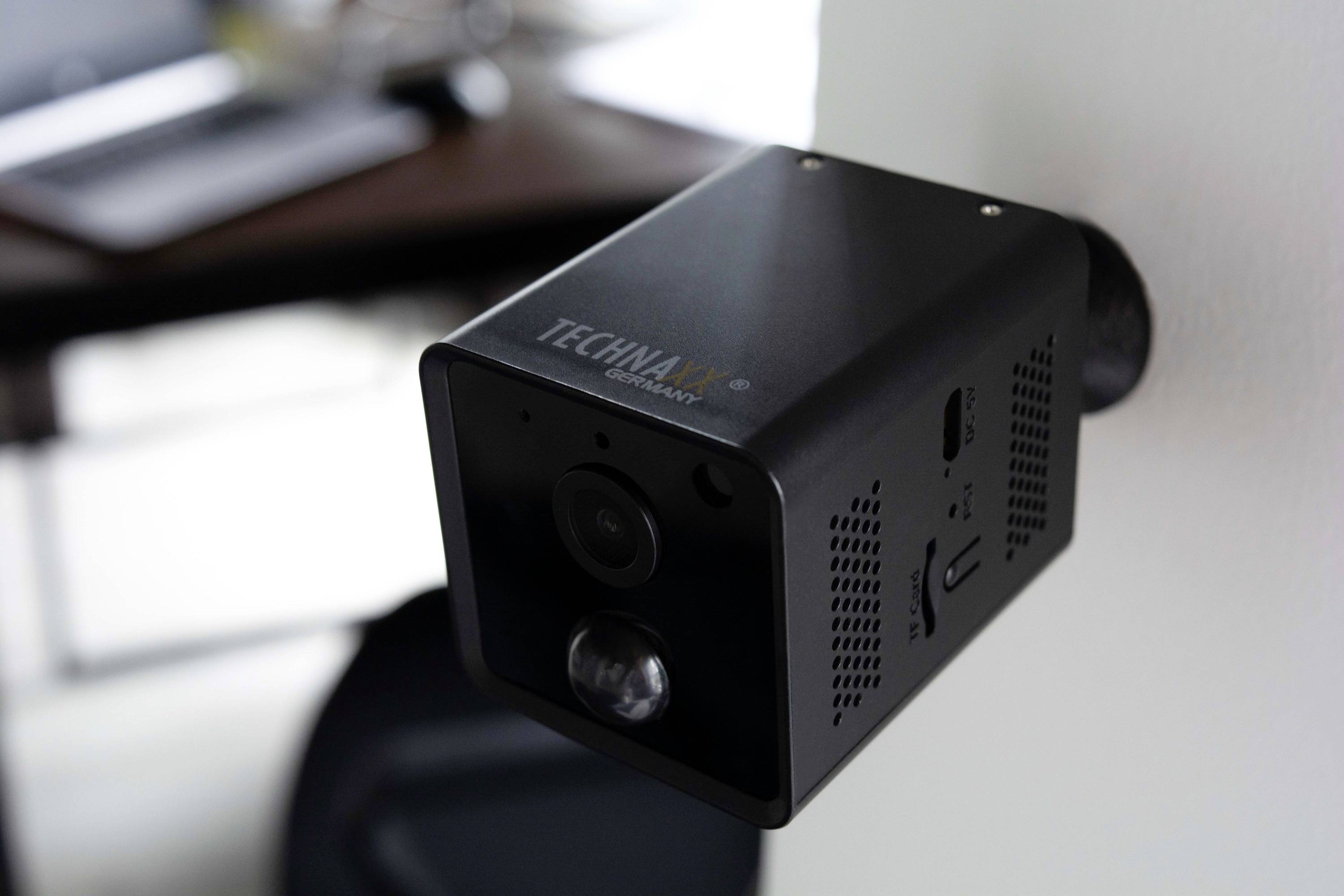 Kamera monitorująca 'Technax' zamontowana na ścianie, w tle nieostry obszar biurka.