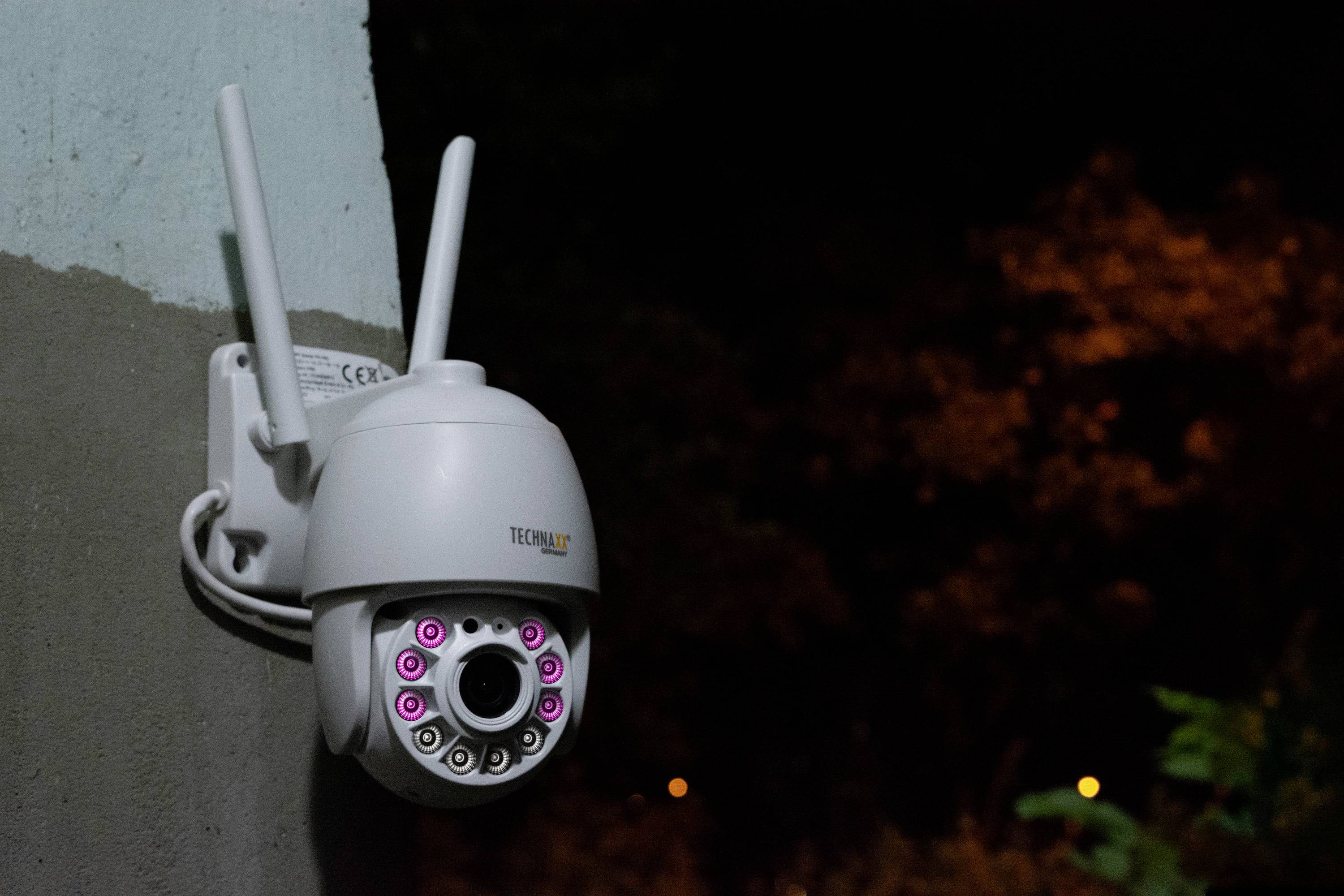 Kamera monitorująca z funkcją widzenia nocnego, zamontowana na ścianie, pokazuje dziewięć świecących świateł wokół obiektywu, na nocnym, oświetlonym tle.